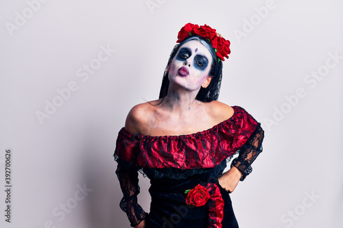 Young woman wearing mexican day of the dead makeup looking at the camera blowing a kiss on air being lovely and sexy. love expression.