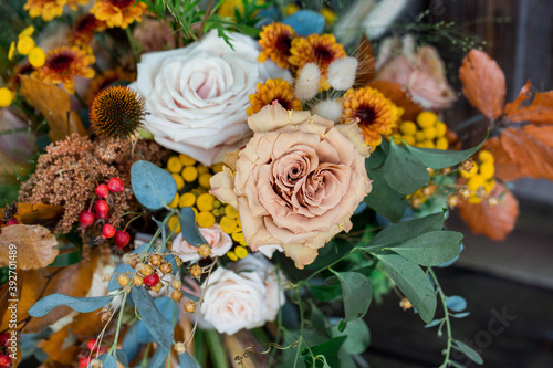 close up of fall flower arrangement with orange, beige, yellow and greenery in lush arrangement