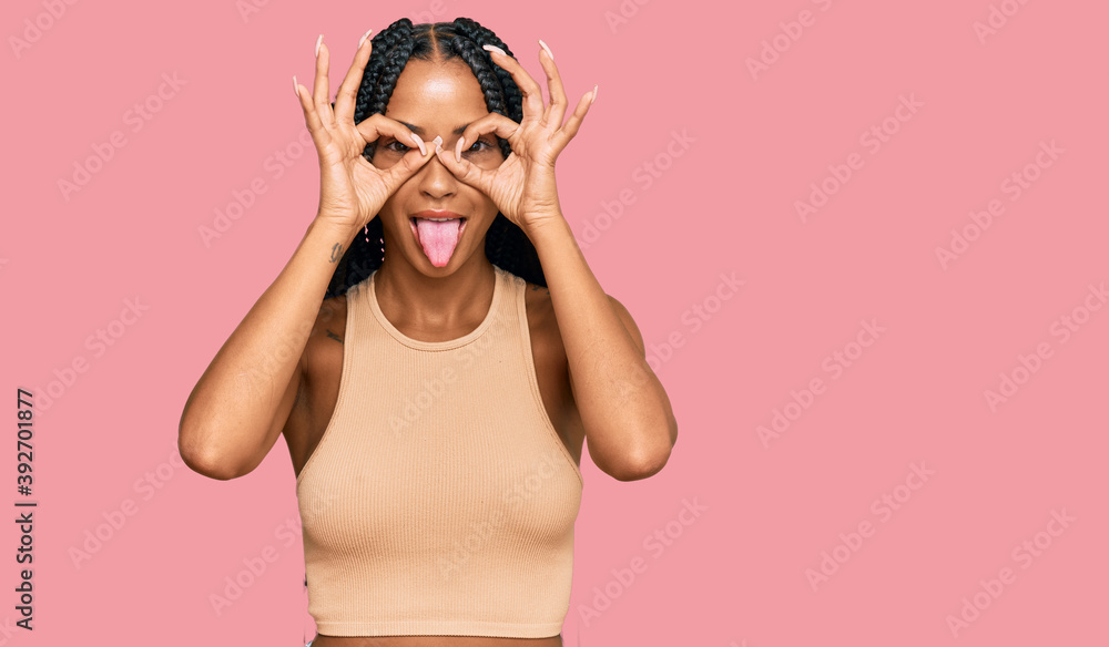 Beautiful hispanic woman wearing casual clothes doing ok gesture like binoculars sticking tongue out, eyes looking through fingers. crazy expression.