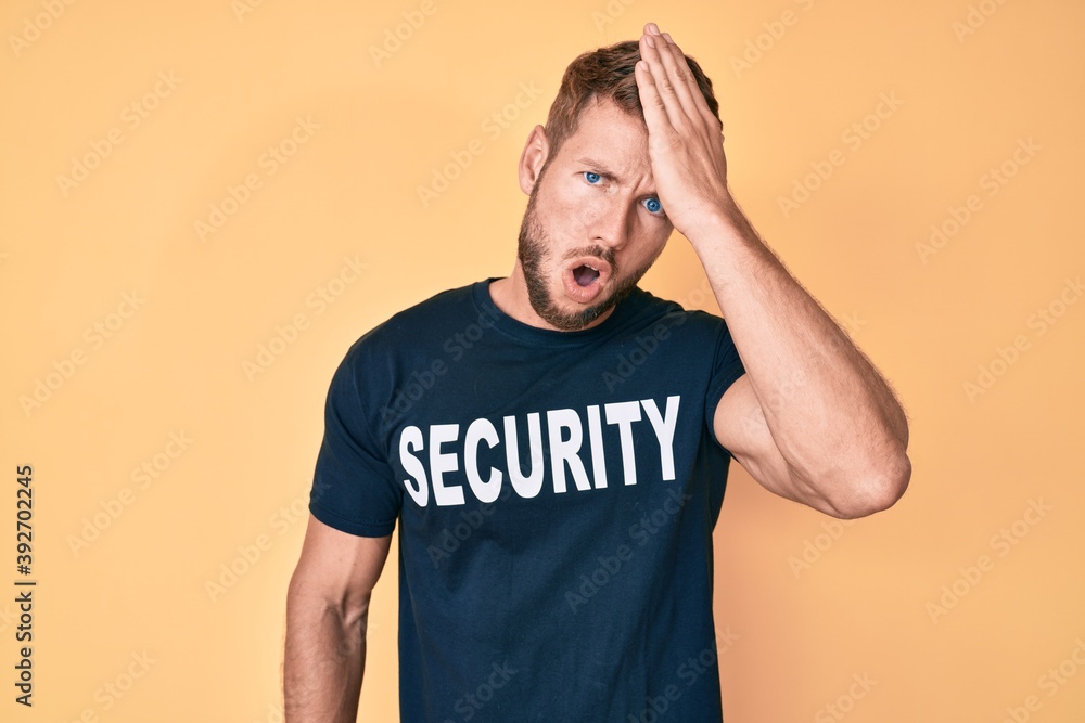 Young caucasian man wearing security t shirt surprised with hand on head for mistake, remember error. forgot, bad memory concept. Young caucasian man wearing security t shirt surprised with hand on head for mistake, remember error. forgot, bad memory concept.