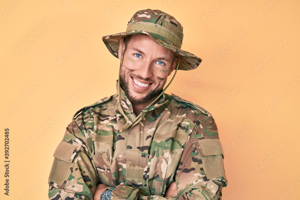 Young caucasian man wearing camouflage army uniform happy face smiling with crossed arms looking at the camera. positive person. Young caucasian man wearing camouflage army uniform happy face smiling with crossed arms looking at the camera. positive person.