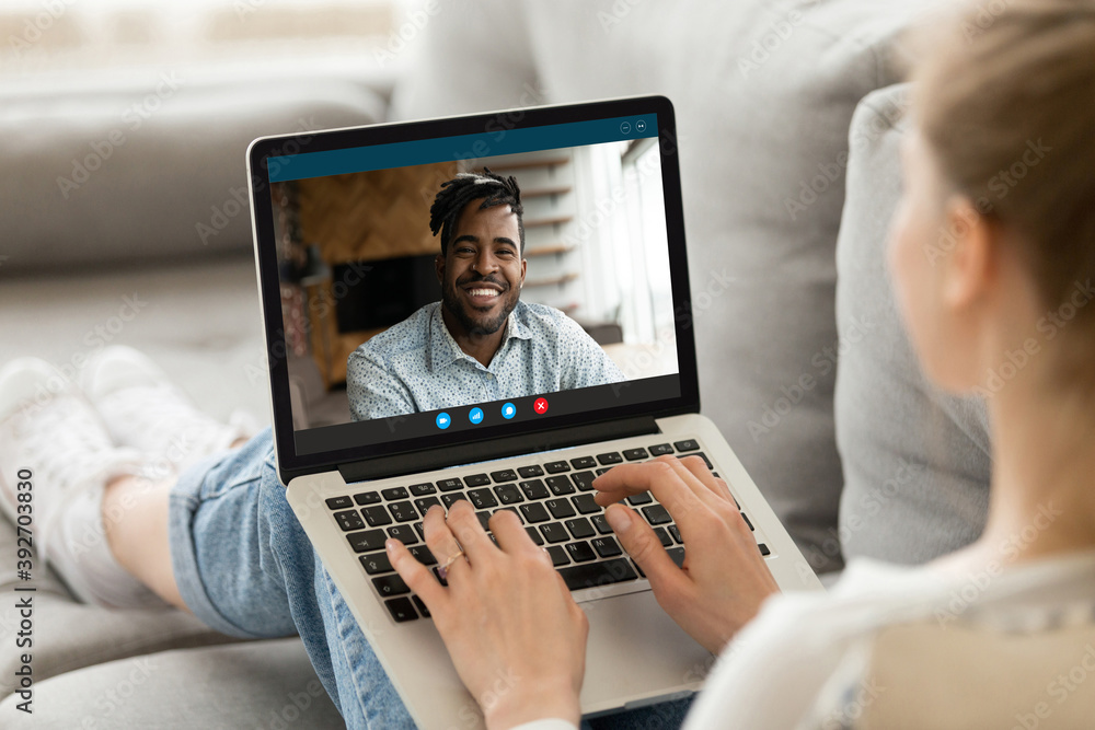 Happy young european woman relaxing on sofa, holding web camera video call with smiling handsome african american boyfriend, using computer software application, distant communication concept. Happy young european woman relaxing on sofa, holding web camera video call with smiling handsome african american boyfriend, using computer software application, distant communication concept.
