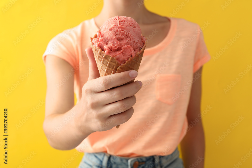 Woman holding pink ice cream in wafer cone on yellow background, closeup