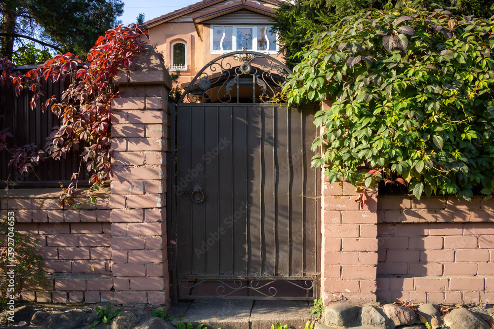 A brown metal gate in a pink brick fence. Entrance from the street