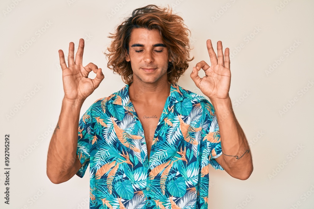 Young hispanic man wearing summer shirt relax and smiling with eyes closed doing meditation gesture with fingers. yoga concept. Young hispanic man wearing summer shirt relax and smiling with eyes closed doing meditation gesture with fingers. yoga concept.