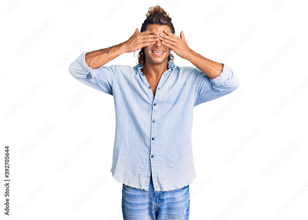 Young hispanic man wearing summer style covering eyes with hands smiling cheerful and funny. blind concept. Young hispanic man wearing summer style covering eyes with hands smiling cheerful and funny. blind concept.