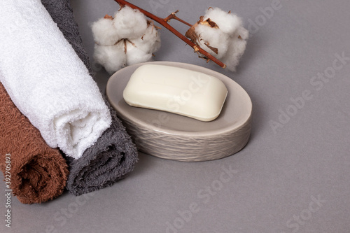 Multicolored towels, soap and cotton branch on a gray background.