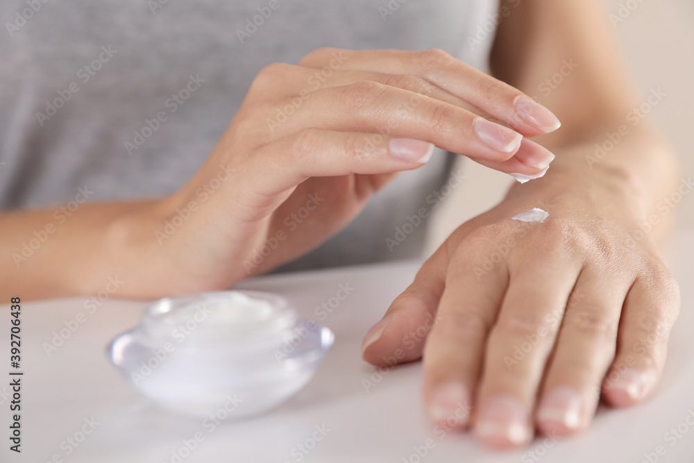Young woman applying hand cream at table, closeup Young woman applying hand cream at table, closeup