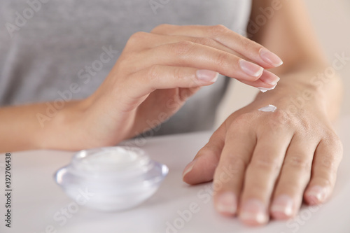 Young woman applying hand cream at table  closeup