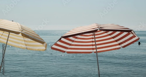 Two colorful striped umbrellas, yellow and red on a beach. Sunny day vacation footage in front of ocean water with calm sea. Horizon holiday tropical shot with relaxation, meditation, resort sun mood