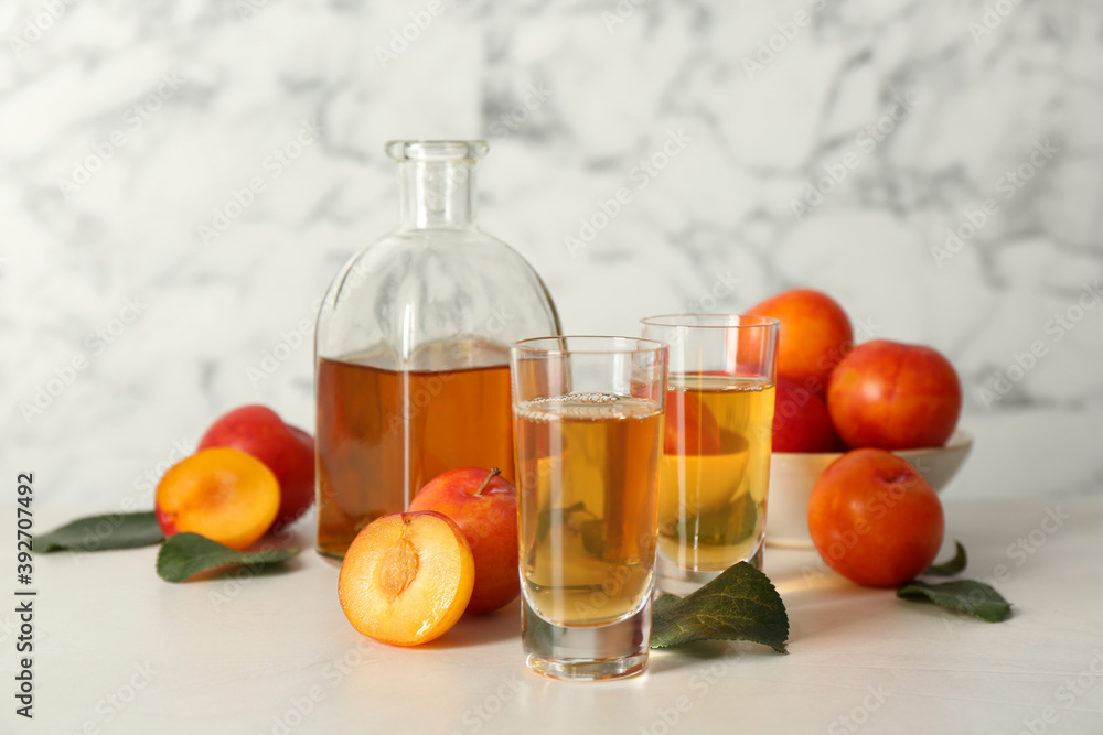 Delicious plum liquor and ripe fruits on white table. Homemade strong alcoholic beverage Delicious plum liquor and ripe fruits on white table. Homemade strong alcoholic beverage