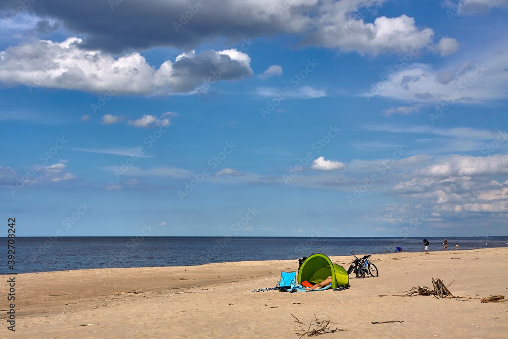 Unrecognizable tourist resting in a green beach tent on a Baltic Sea beach in summer.