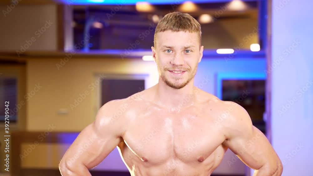 Close up portrait of a confident muscular shirtless bodybuilder guy looking at camera. Young strong male fitness trainer posing in gym. Attractive sexy person smiles. Sports club and exercise machines Close up portrait of a confident muscular shirtless bodybuilder guy looking at camera. Young strong male fitness trainer posing in gym. Attractive sexy person smiles. Sports club and exercise machines