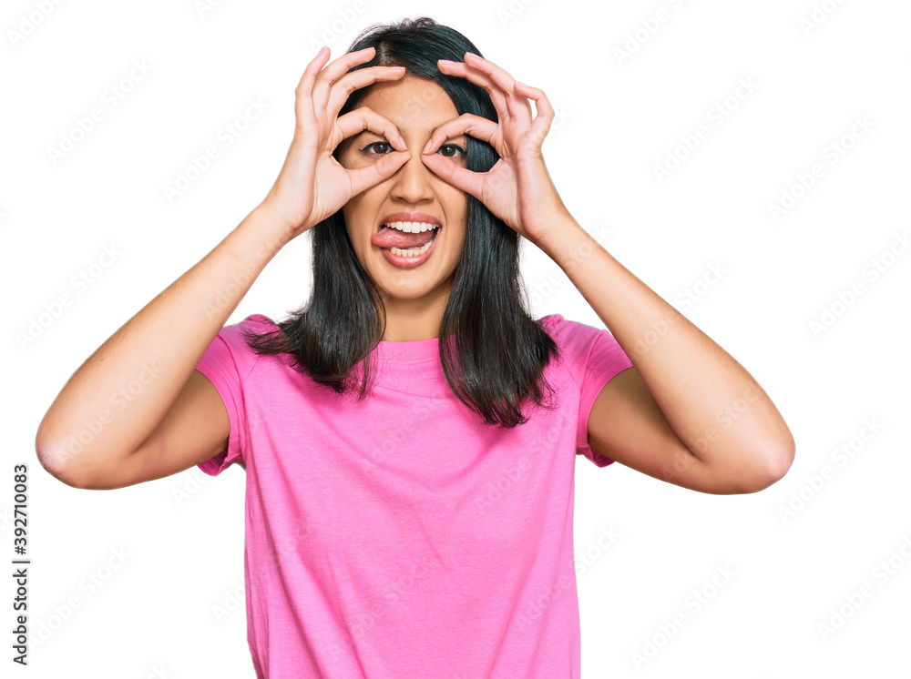 Beautiful asian young woman wearing casual pink t shirt doing ok gesture like binoculars sticking tongue out, eyes looking through fingers. crazy expression. Beautiful asian young woman wearing casual pink t shirt doing ok gesture like binoculars sticking tongue out, eyes looking through fingers. crazy expression.