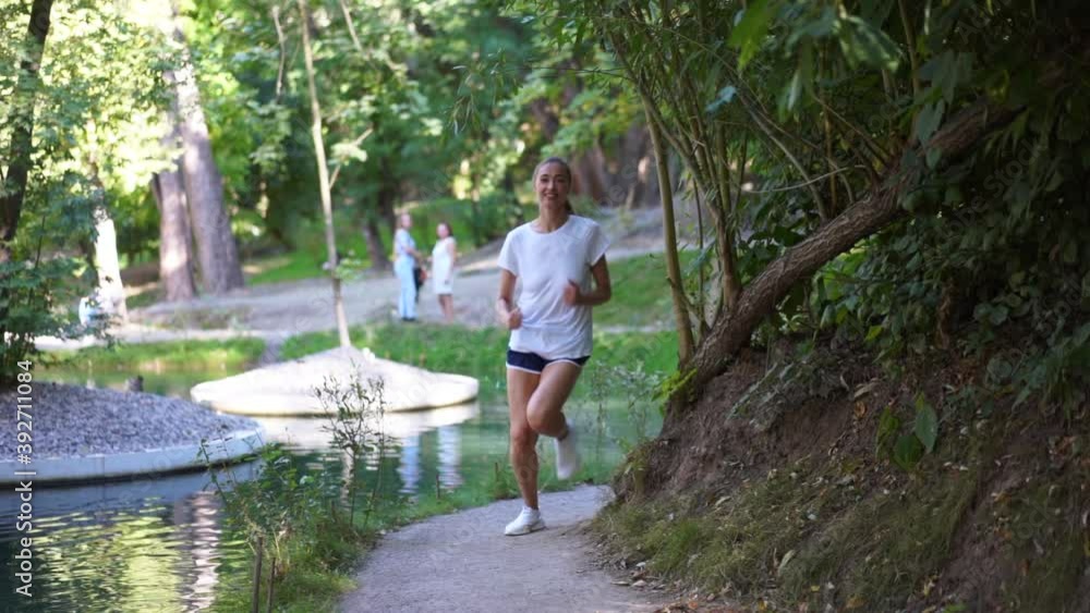 Woman running asphalt road summer park lake Active sporty caucasian female morning workout Healthy lifestyle concept. Athletic person sportswear exercises full length Slow motion Woman running asphalt road summer park lake Active sporty caucasian female morning workout Healthy lifestyle concept. Athletic person sportswear exercises full length Slow motion