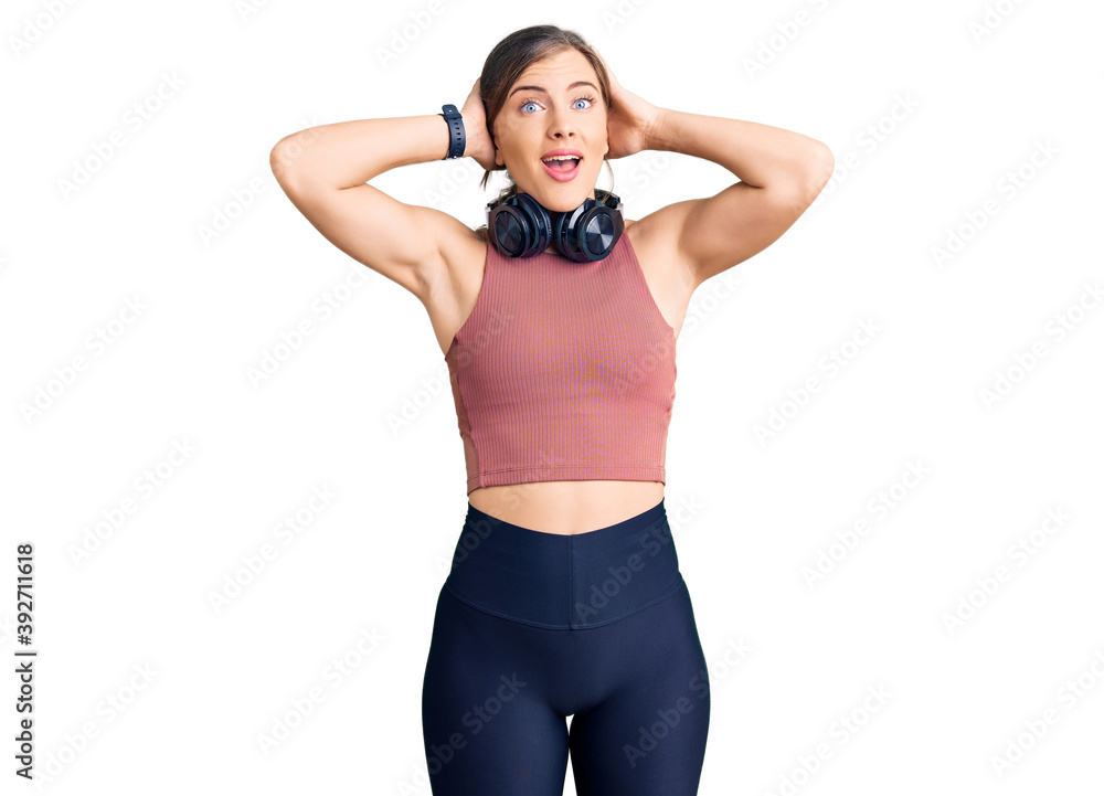 Beautiful caucasian young woman wearing gym clothes and using headphones crazy and scared with hands on head, afraid and surprised of shock with open mouth Beautiful caucasian young woman wearing gym clothes and using headphones crazy and scared with hands on head, afraid and surprised of shock with open mouth
