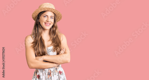 Beautiful caucasian young woman wearing summer hat happy face smiling with crossed arms looking at the camera. positive person.
