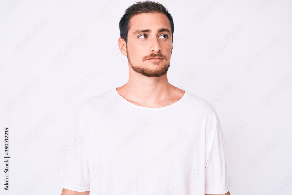 Fototapeta premium Young handsome man wearing casual white tshirt smiling looking to the side and staring away thinking.