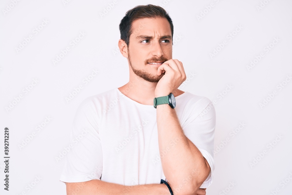 Young handsome man wearing casual white tshirt looking stressed and nervous with hands on mouth biting nails. anxiety problem. Young handsome man wearing casual white tshirt looking stressed and nervous with hands on mouth biting nails. anxiety problem.