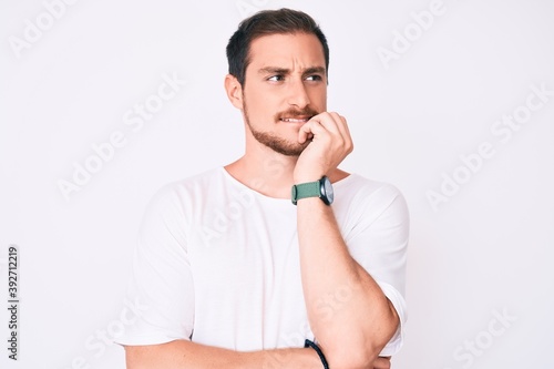 Young handsome man wearing casual white tshirt looking stressed and nervous with hands on mouth biting nails. anxiety problem.