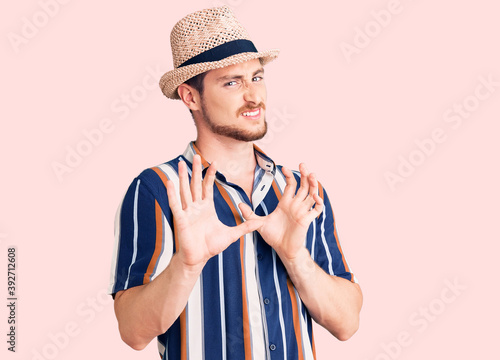 Foto Young handsome caucasian man wearing summer hat disgusted expression, displeased and fearful doing disgust face because aversion reaction