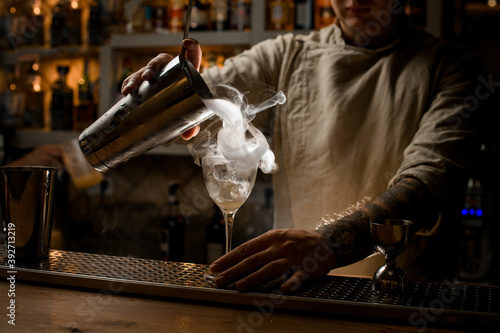 view of male bartender pouring steaming drink from shaker cup into wine glass