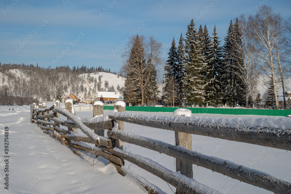 Winter village in the mountains. Trees and fences are covered with snow and frost. Winter village in the mountains. Trees and fences are covered with snow and frost.