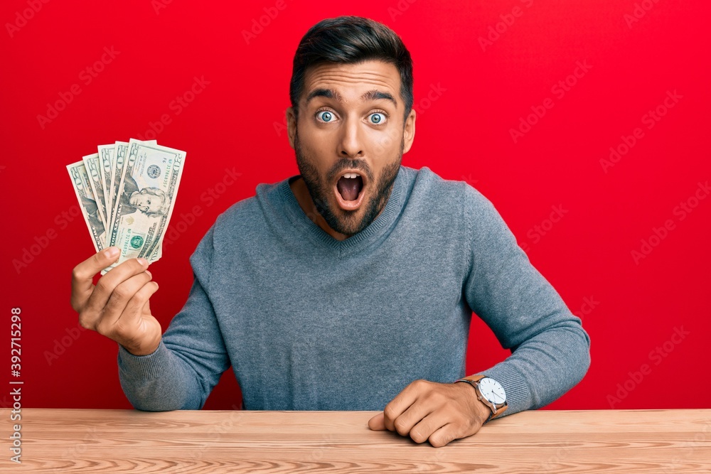 Handsome hispanic man holding 20 dollars banknotes scared and amazed with open mouth for surprise, disbelief face Handsome hispanic man holding 20 dollars banknotes scared and amazed with open mouth for surprise, disbelief face