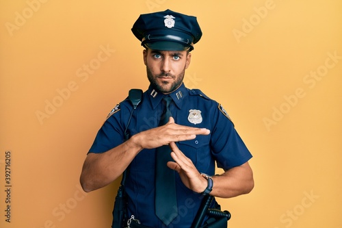 Handsome hispanic man wearing police uniform doing time out gesture with hands, frustrated and serious face photo