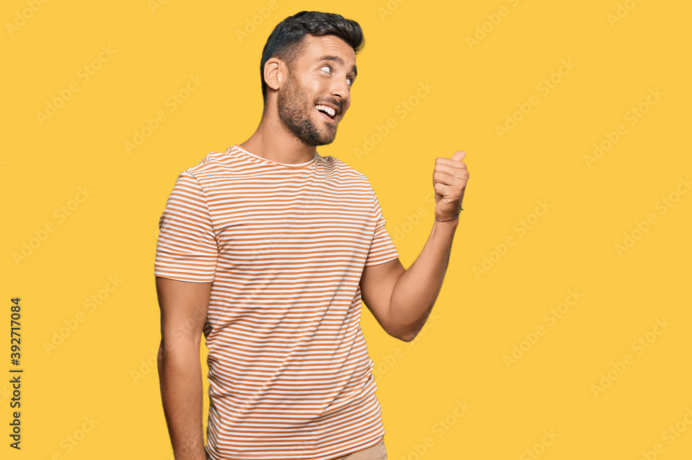 Handsome hispanic man wearing casual clothes smiling with happy face looking and pointing to the side with thumb up. Handsome hispanic man wearing casual clothes smiling with happy face looking and pointing to the side with thumb up.