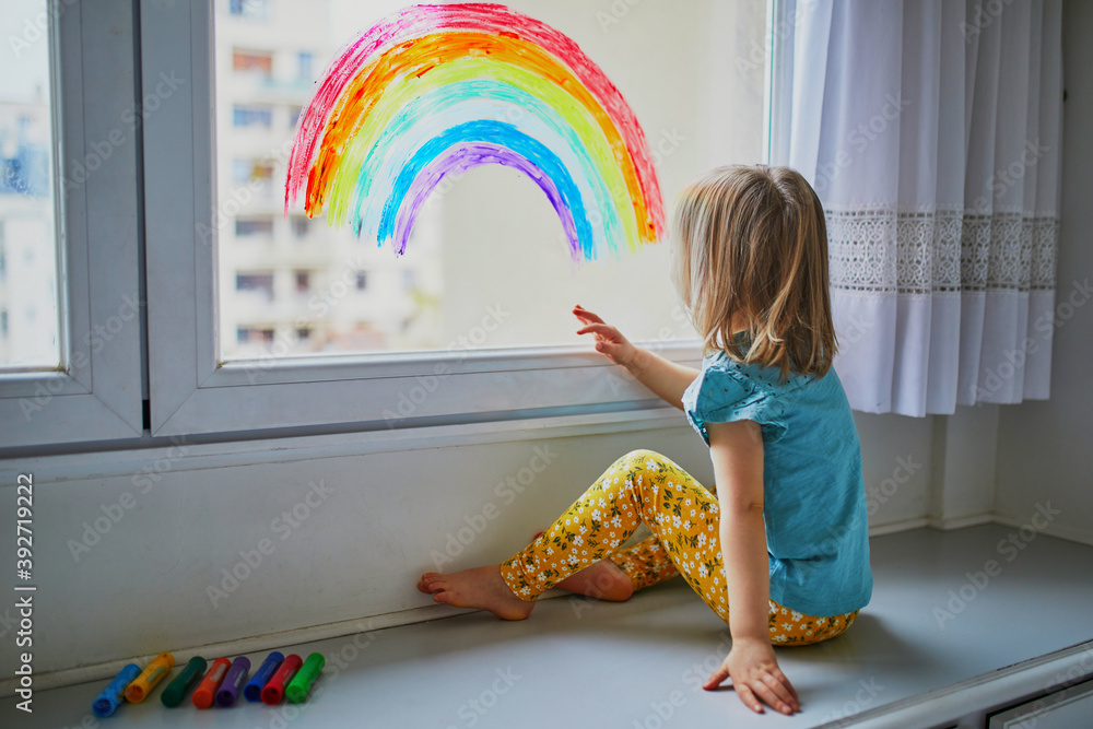 Fotografija Adorable toddler girl drawing rainbow on window glass
