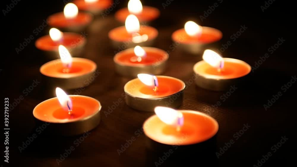 Many candles burning in the dark, Burning candle flame in the wind, Background of small orange candles Many candles burning in the dark, Burning candle flame in the wind, Background of small orange candles