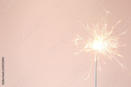 Bright burning sparkler on pink background, closeup. Space for text