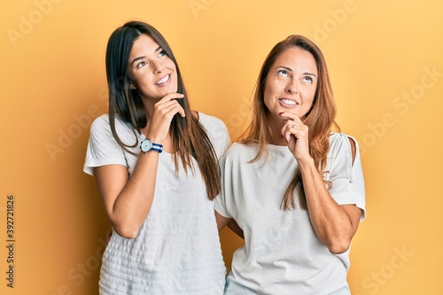 Hispanic family of mother and daughter wearing casual white tshirt with hand on chin thinking about question, pensive expression. smiling and thoughtful face. doubt concept.