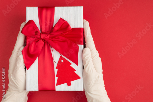 Merry Christmas concept. Top pov above overhead close up view photo of hands in disposable white rubber latex gloves holding big giftbox with card isolated background with empty blank space