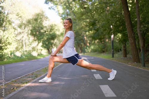 Woman runner stretching legs before exercising summer park morning