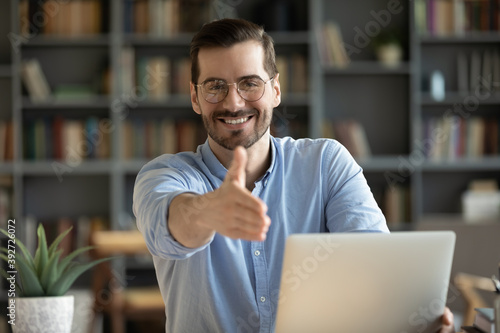 Valokuva Human resource agent male recruiter sit at desk extends his hand to camera for handshake greeting applicant showing polite gesture start job interview in modern office