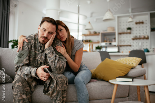 Depressed soldier sitting on sofa with his wife. Young marine having PTSD...
