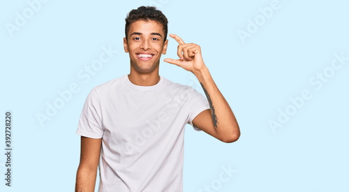Young handsome african american man wearing casual white tshirt smiling and confident gesturing with hand doing small size sign with fingers looking and the camera. measure concept.