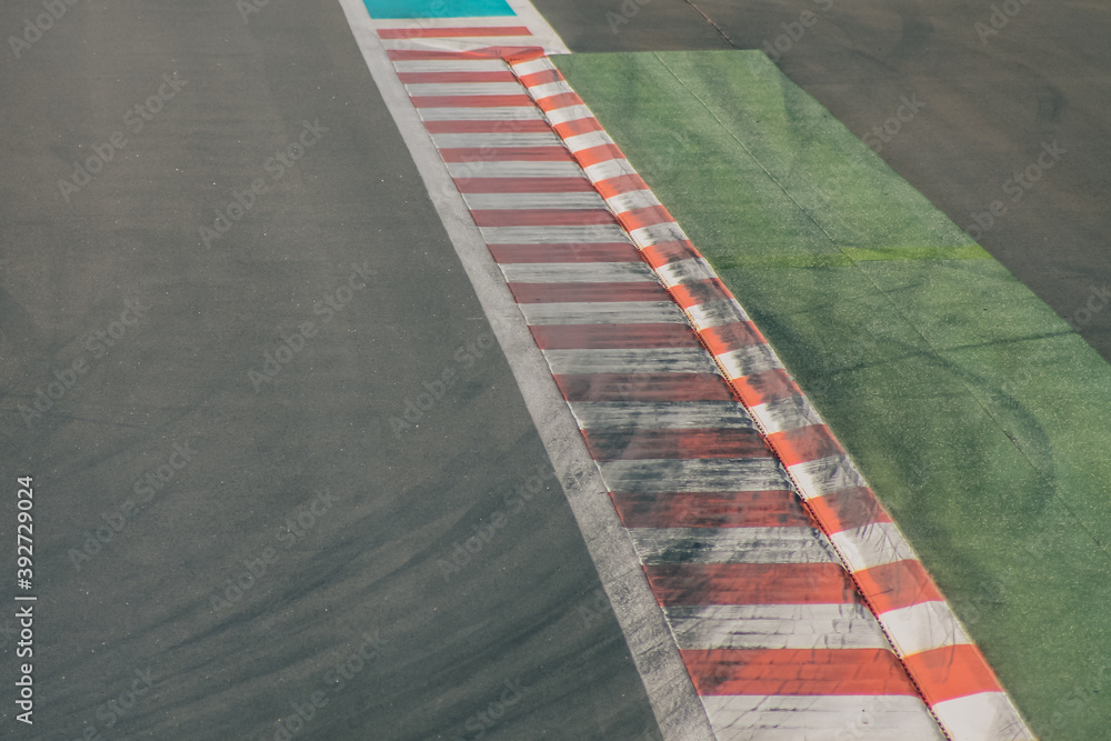Edge of a racetrack curve on the exit, with visible skid marks or rubber imprints of tires over the red and white field.