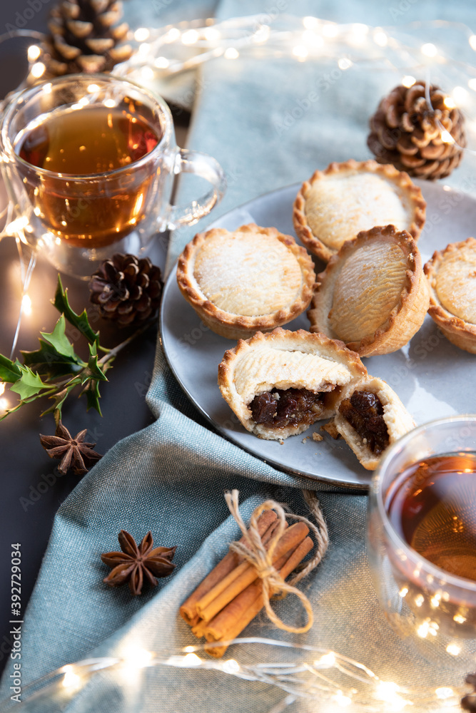 mince pies on a plate served with black tea. A mince pie is a traditional Christmas sweet pie, filled with a mixture of dried fruits and spices. mince pies on a plate served with black tea. A mince pie is a traditional Christmas sweet pie, filled with a mixture of dried fruits and spices.