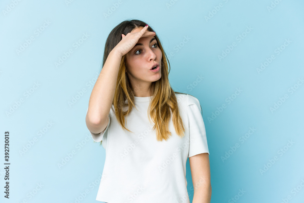 Young caucasian woman isolated on blue background looking far away keeping hand on forehead.