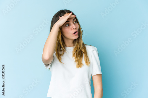 Young caucasian woman isolated on blue background looking far away keeping hand on forehead.