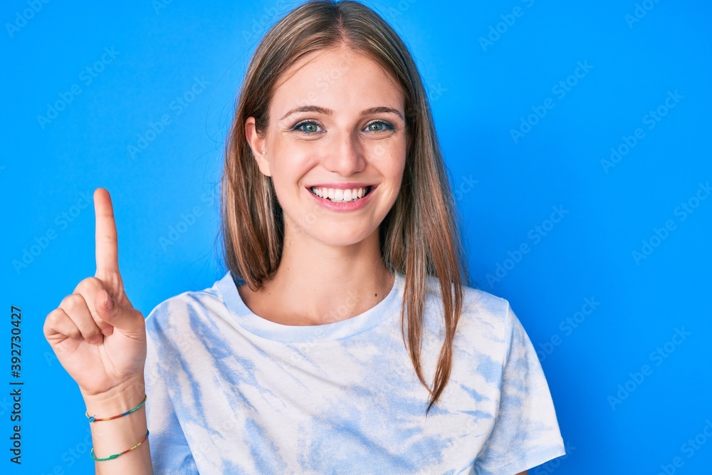 Young blonde girl wearing casual clothes smiling with an idea or question pointing finger up with happy face, number one Young blonde girl wearing casual clothes smiling with an idea or question pointing finger up with happy face, number one