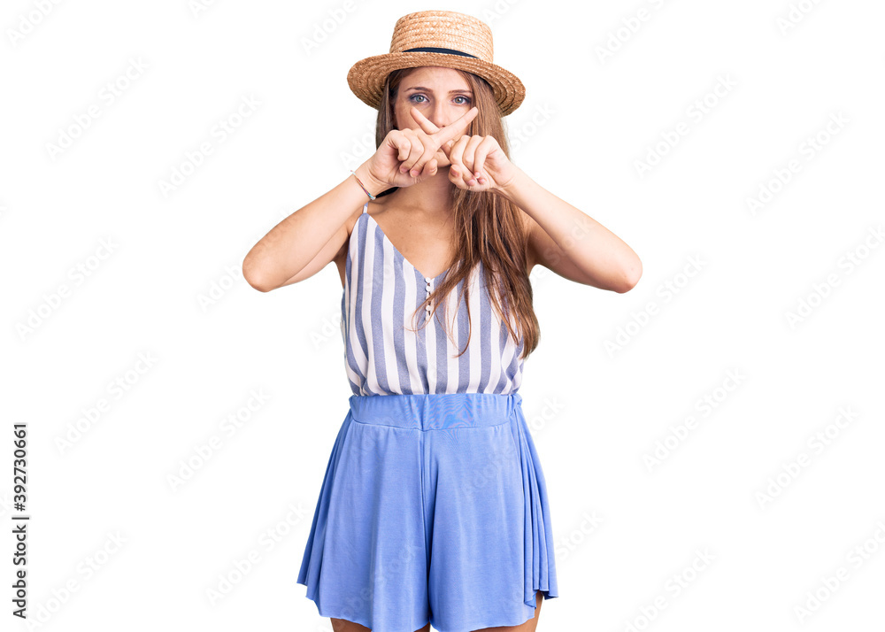 Young beautiful blonde woman wearing summer hat rejection expression crossing fingers doing negative sign Young beautiful blonde woman wearing summer hat rejection expression crossing fingers doing negative sign