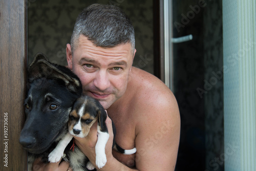 close-up portrait of happy senior man looking at camera on a home background of window. Man holding and hugging beagle dog and Eastern European Shepherd. Smiling, enjoying good day with pet