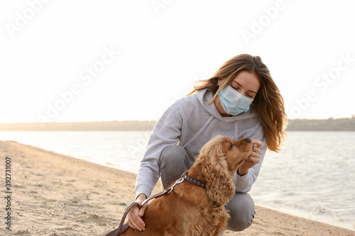 Woman in protective mask with English Cocker Spaniel on beach. Walking dog during COVID-19 pandemic