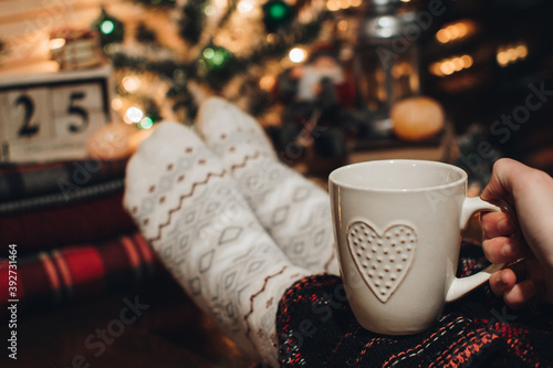 Feet in Christmas socks. Close up on feet. Winter and Christmas holidays concept. The cup of hot drink. Cozy scene. Background with christmas decor. Christmas background.