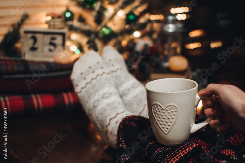 Feet in Christmas socks. Close up on feet. Winter and Christmas holidays concept. The cup of hot drink. Cozy scene. Background with christmas decor. Christmas background.