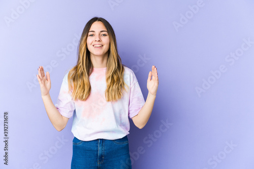 Young caucasian woman isolated on purple background holding something little with forefingers, smiling and confident.